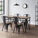 Dining area with wooden table and black metal chairs against a white brick wall.