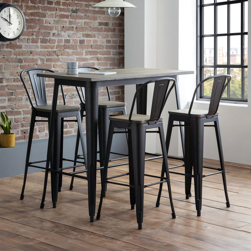 Set of black metal bar stools around a dining table in a modern room with brick wall and large window.