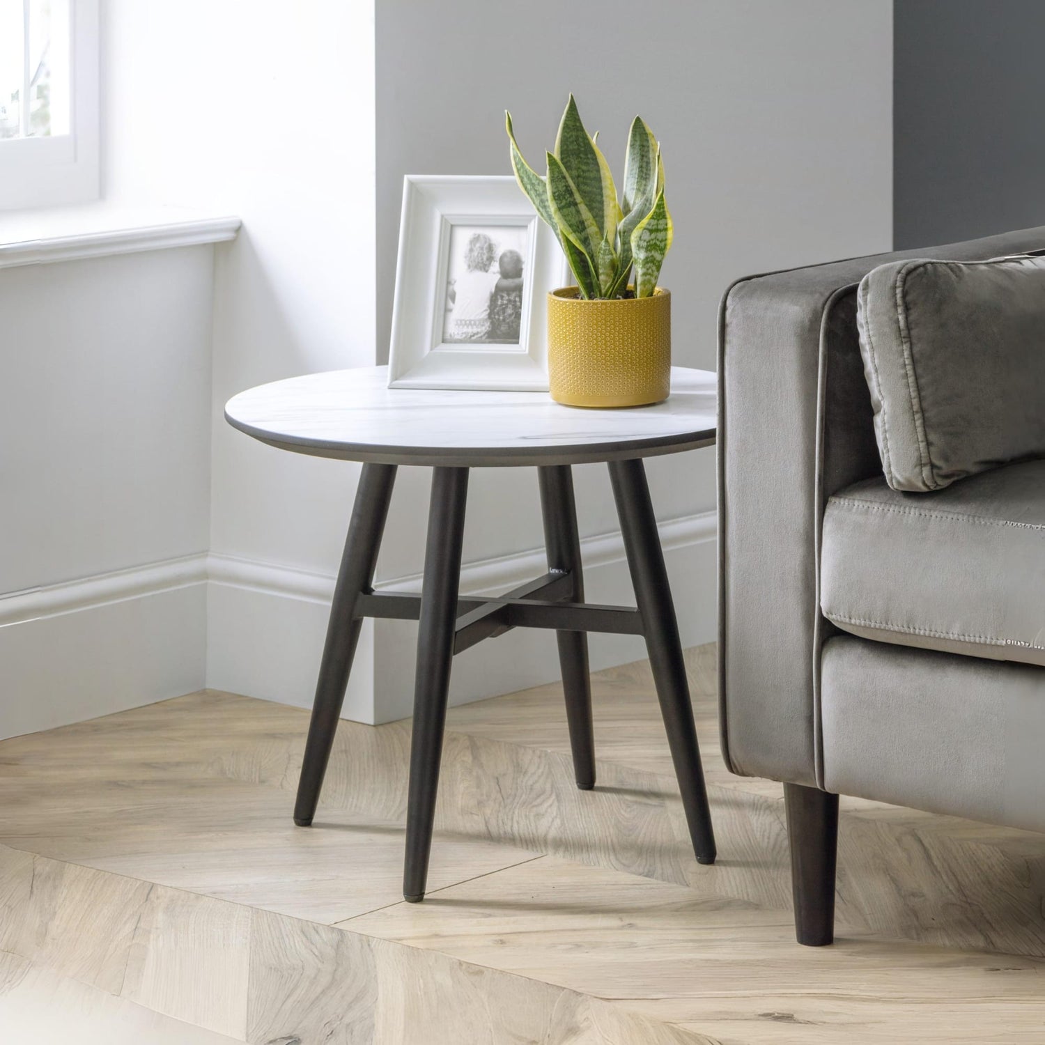 Round side table with a plant and photo frame next to a gray sofa in a living room.
