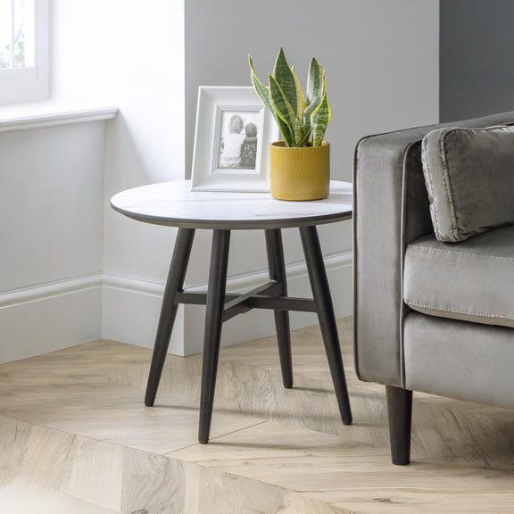 Round side table with a plant and photo frame next to a gray sofa in a living room.