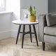 Round side table with a plant and photo frame next to a gray sofa in a living room.