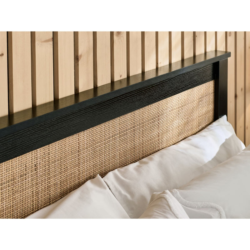 Bed with a black and wicker headboard against a wooden wall.