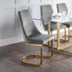 Gray chair with gold legs in front of a glass dining table with white plates and glasses.