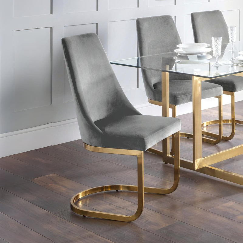 Gray chair with gold legs in front of a glass dining table with white plates and glasses.