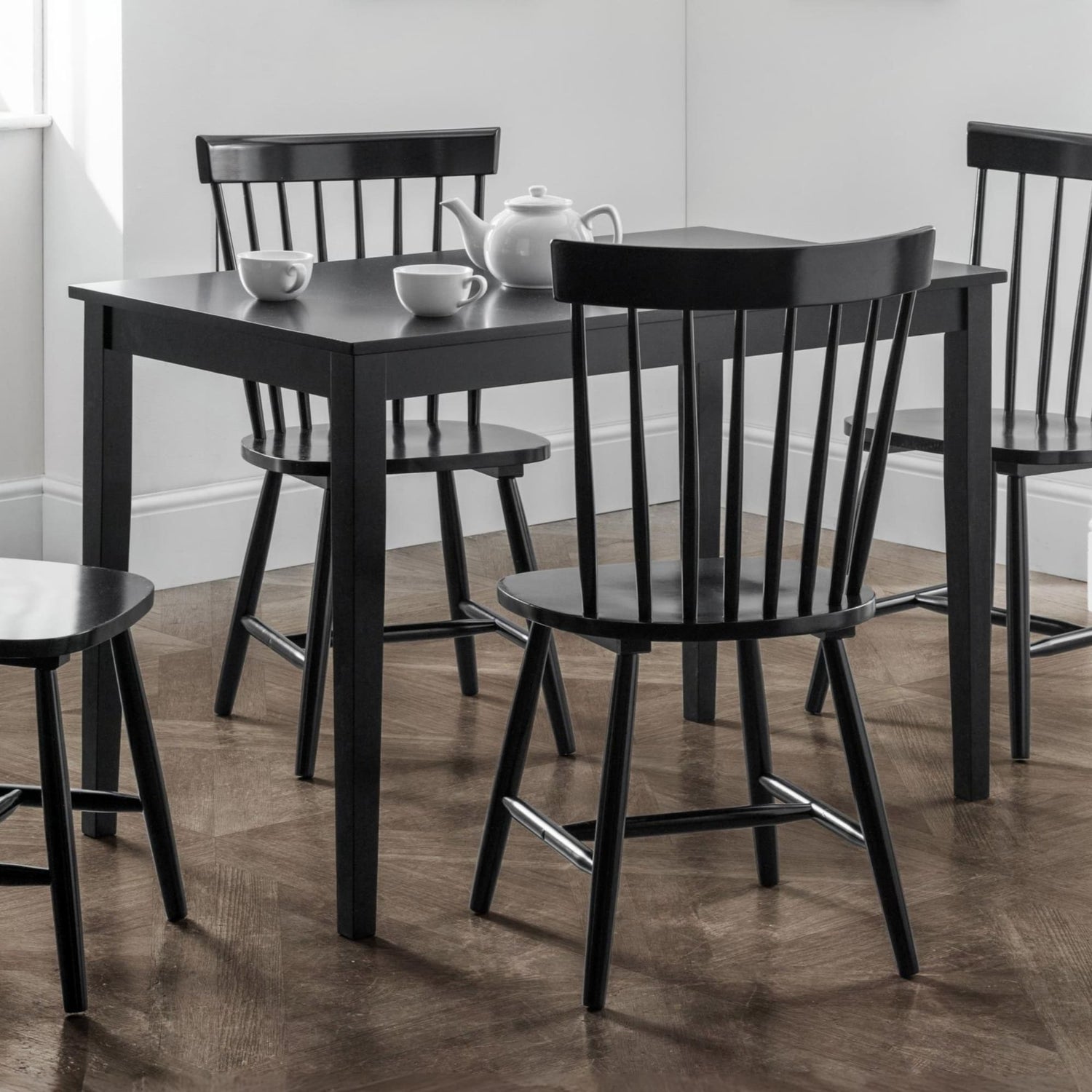 Black dining table with four chairs in a room with white walls and wooden flooring.
