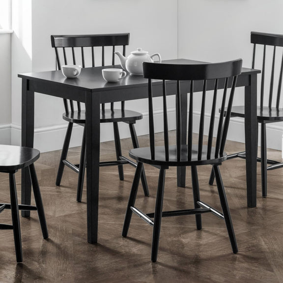 Black dining table with four chairs in a room with white walls and wooden flooring.