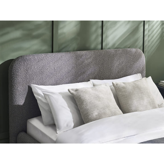 Gray upholstered headboard with white and gray pillows against a neutral wall.