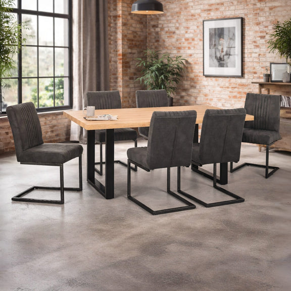 Dining table with six gray chairs in a room with brick walls and large windows.