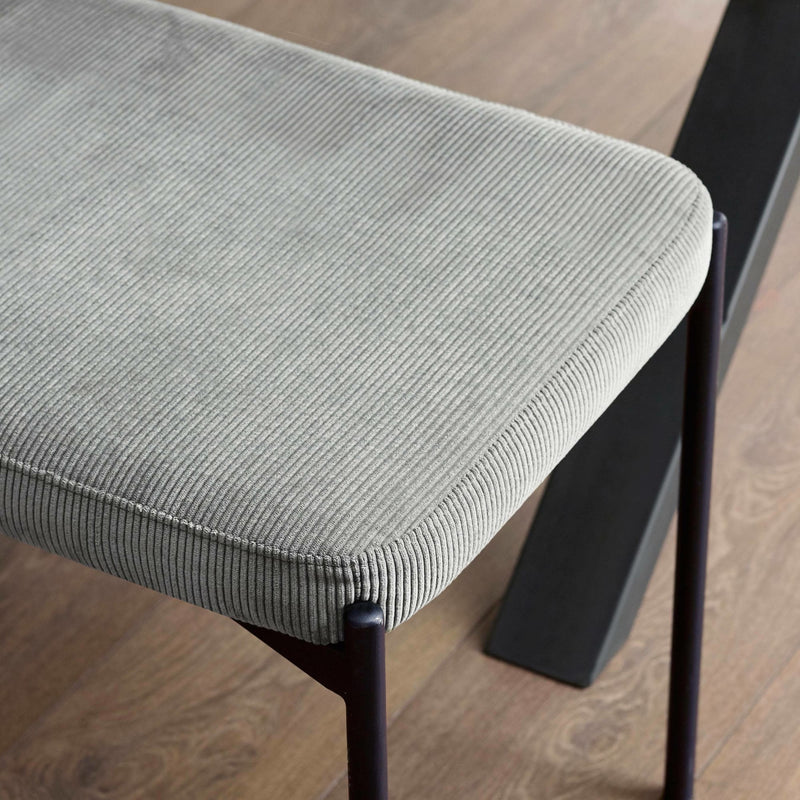 Gray cushioned stool with black metal legs on a wooden floor