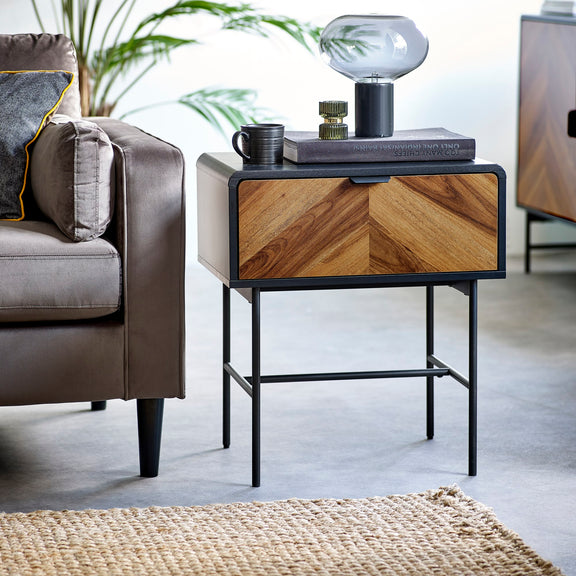 Wooden side table with decorative items next to a gray sofa in a living room setting.