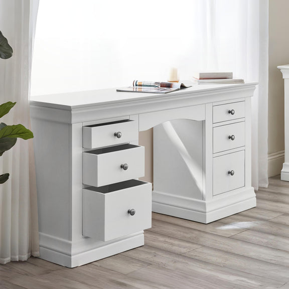 White desk with multiple drawers in a room with curtains and a plant.