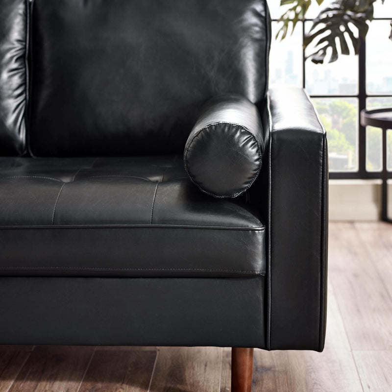 Black leather sofa with a cylindrical pillow in a room with large windows.