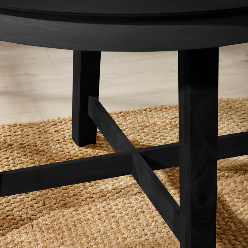Close-up of a black wooden stool on a textured beige rug.