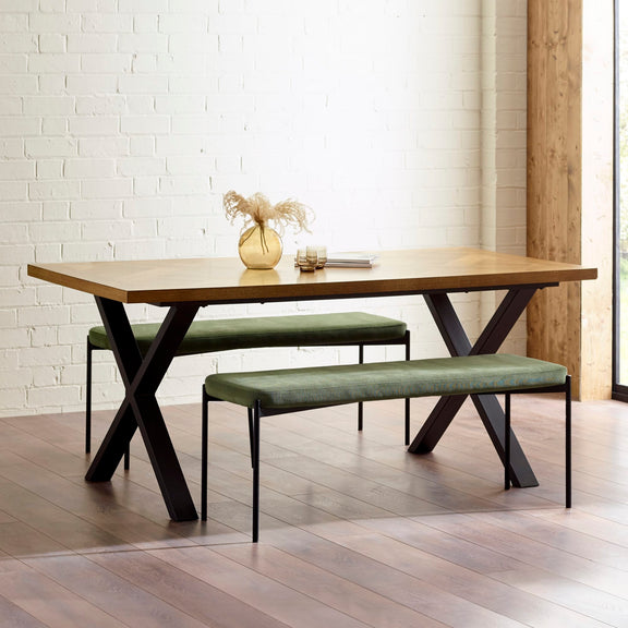 Dining table with X-shaped metal legs and green benches against a white brick wall.