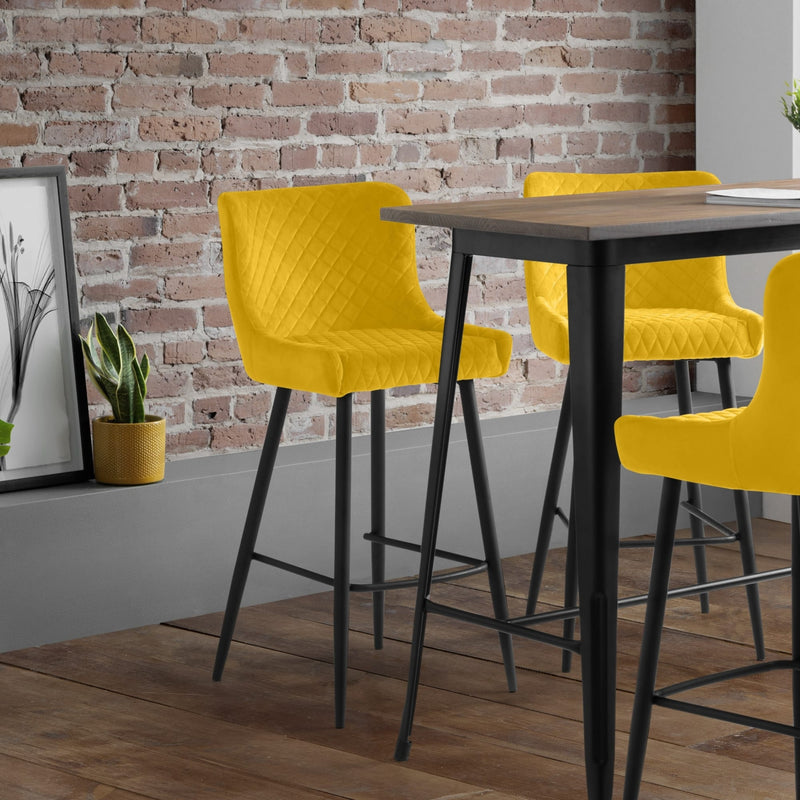 Yellow bar stools around a wooden table against a brick wall.