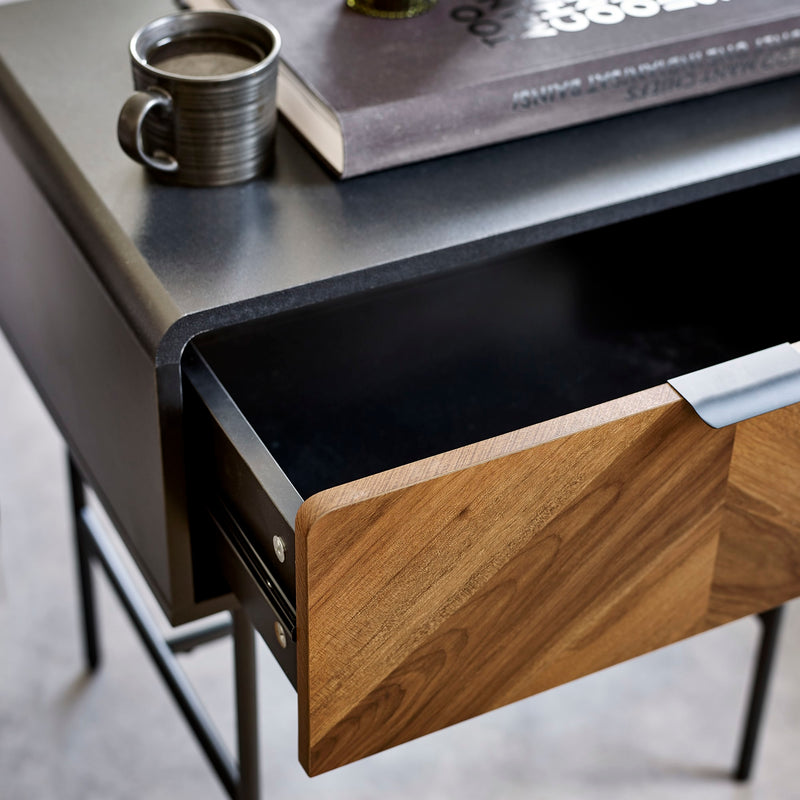 Wooden drawer being pulled out from a black desk with a cup and book on top.