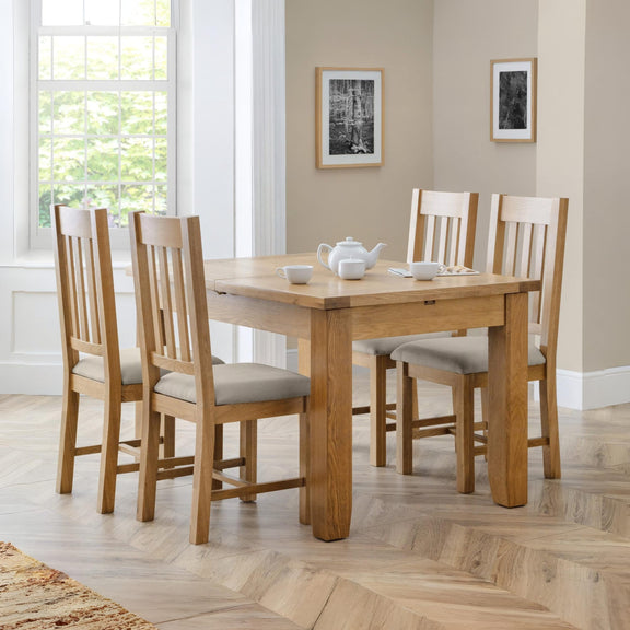 Wooden dining table with four chairs in a room with large windows and framed pictures on the wall.