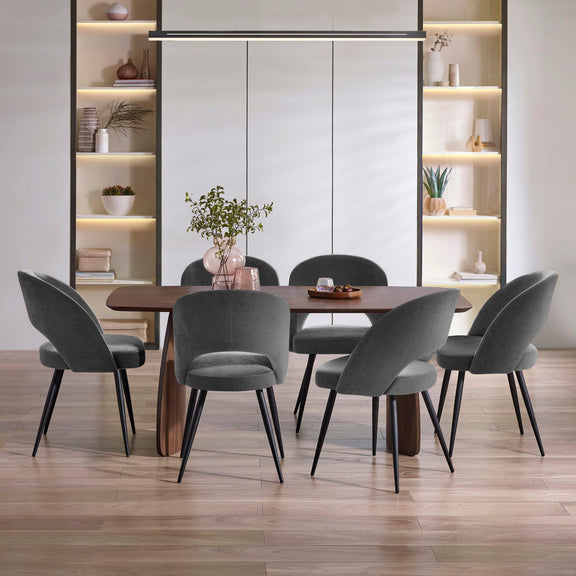Dining room with a wooden table and gray chairs, shelves with decorative items in the background.