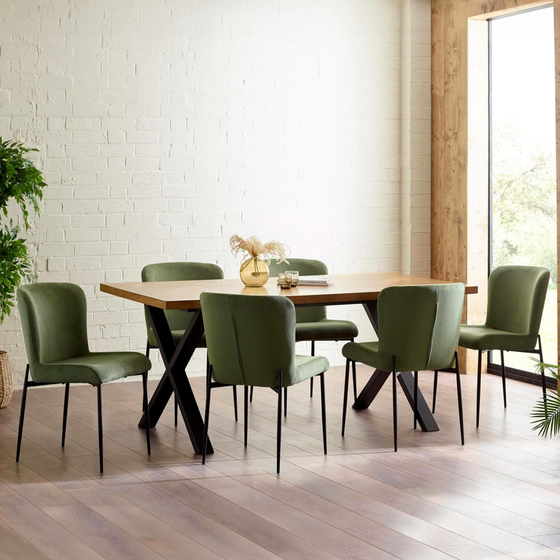 Dining room with a wooden table and green chairs against a white brick wall.