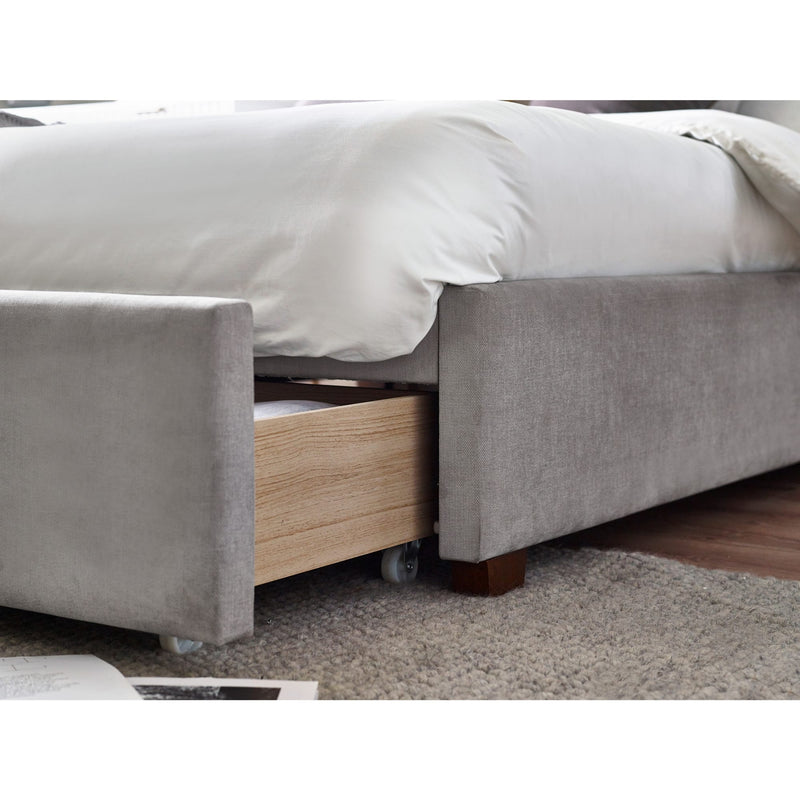Gray upholstered bed with a wooden drawer underneath on a carpeted floor.