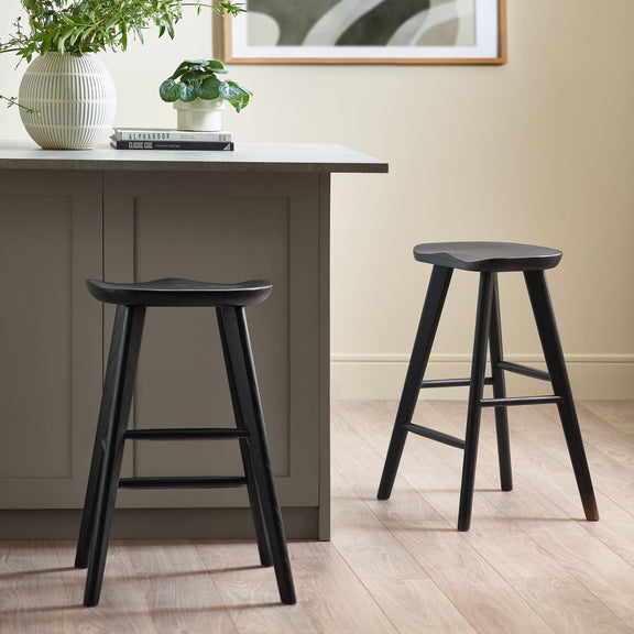 Two black bar stools in front of a gray dining table with a plant and books on it.