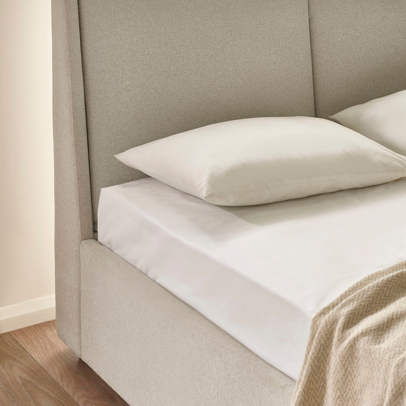Beige upholstered bed with white bedding and a beige blanket