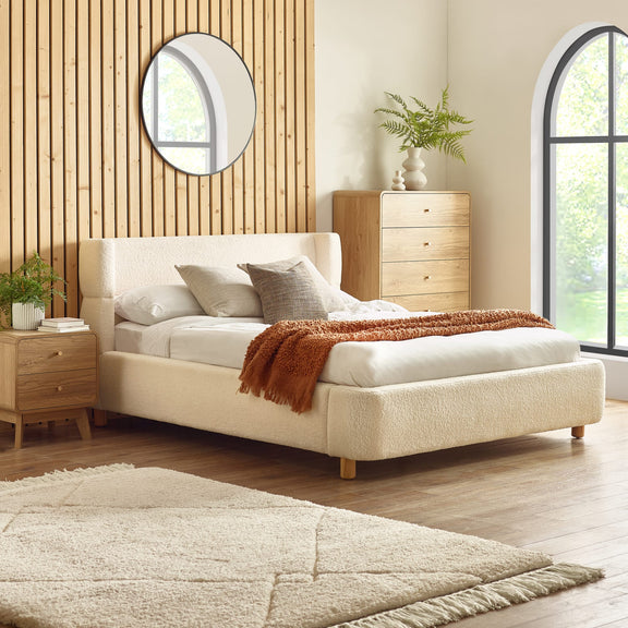 Beige upholstered bed in a bedroom with wooden furniture and decor.