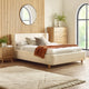 Beige upholstered bed in a bedroom with wooden furniture and decor.