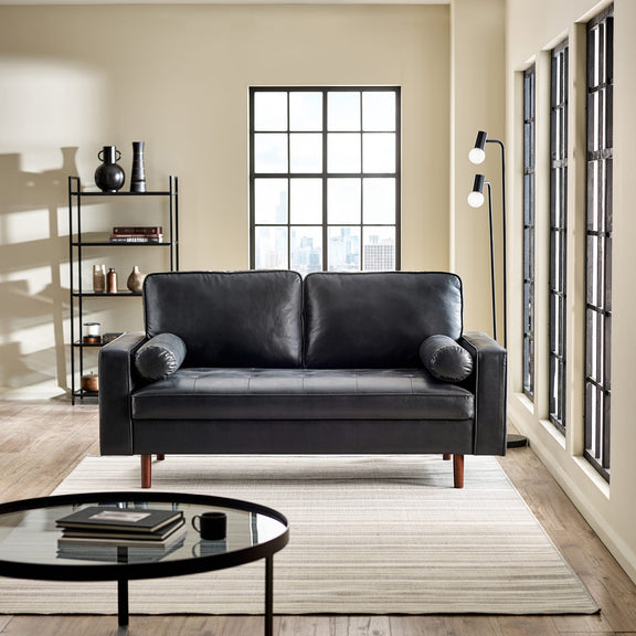 Modern living room with a black leather sofa, round glass coffee table, and decorative shelves.