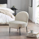Beige armchair in a bedroom setting with books and a cup on a small table.