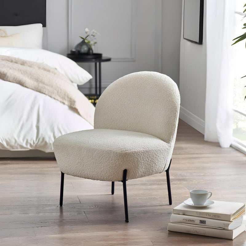 Beige armchair in a bedroom setting with books and a cup on a small table.