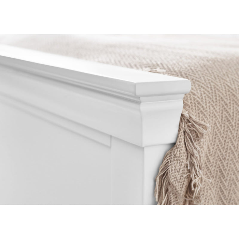 Close-up of a white bed frame with a beige blanket draped over it.