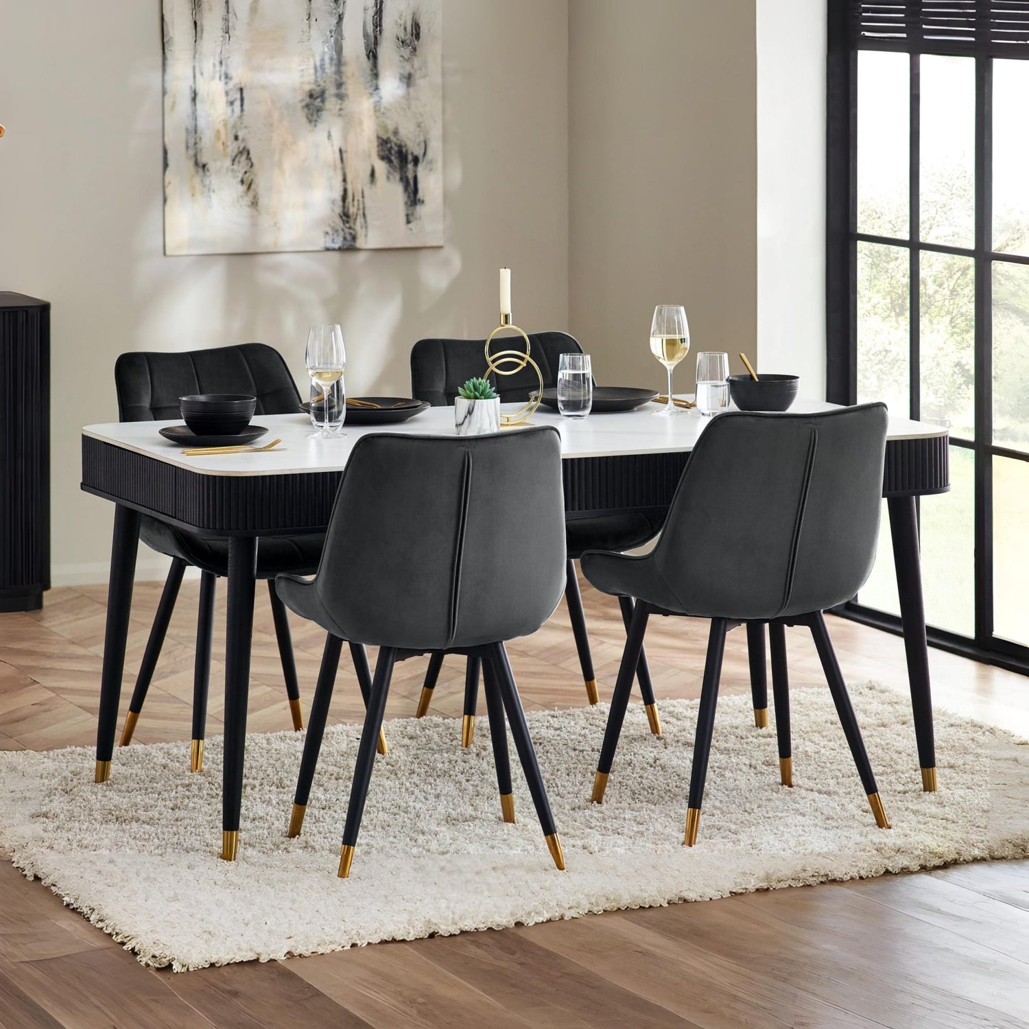 Dining room with a table set for four, black chairs, and a large abstract painting on the wall.