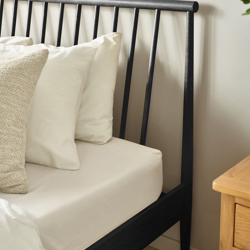 Black metal bed frame with beige pillows and a wooden nightstand.