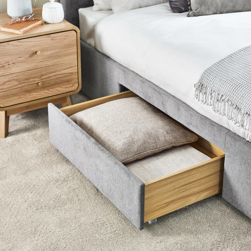 Gray upholstered bed with open drawer revealing a pillow, next to a wooden nightstand.
