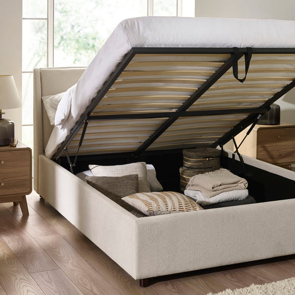 Beige upholstered bed with open storage compartment in a bright room.
