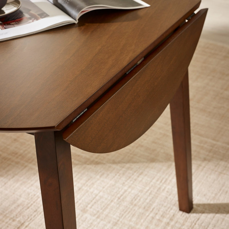 Wooden dining table with a drop leaf extension, featuring an open magazine on top.