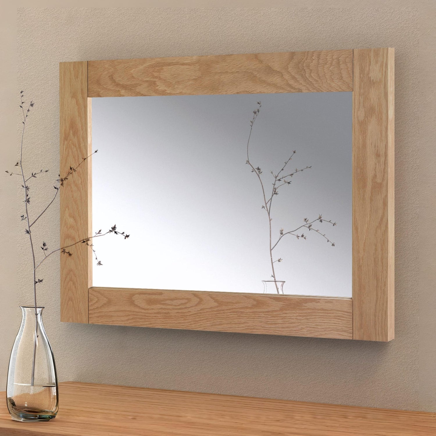 Wooden-framed mirror on a wall with a vase of branches on a table below.