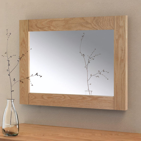 Wooden-framed mirror on a wall with a vase of branches on a table below.