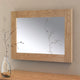 Wooden-framed mirror on a wall with a vase of branches on a table below.