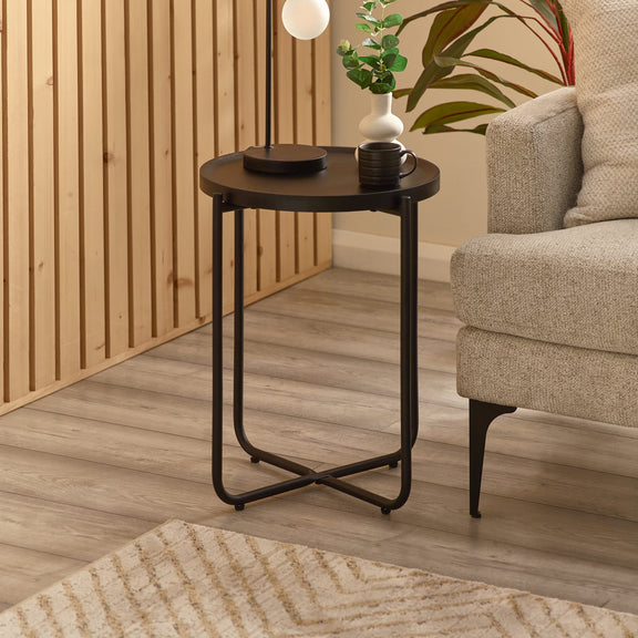 Small round black side table with a plant and cup in a living room setting.