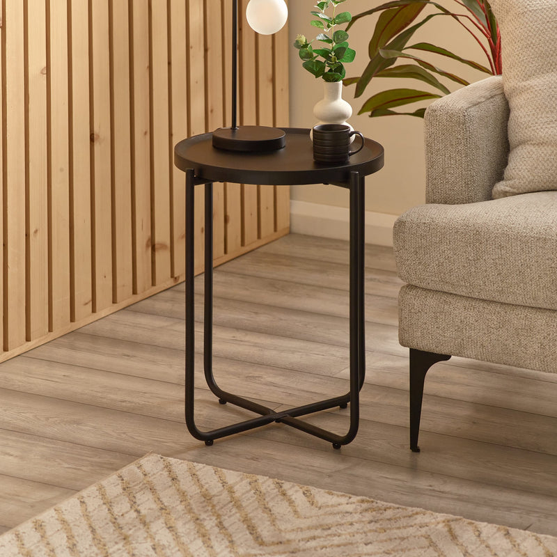 Small round black side table with a plant and cup in a living room setting.