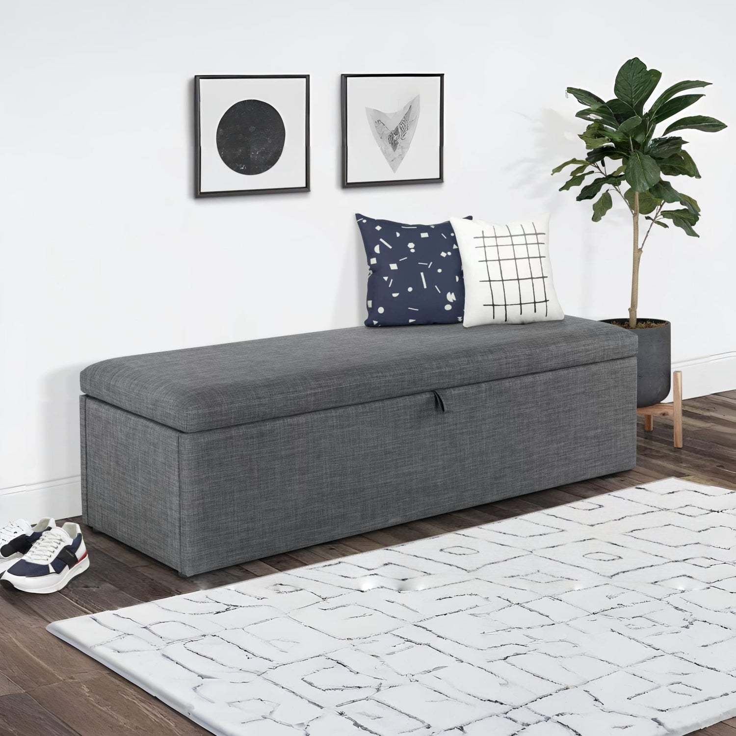 Gray upholstered bench with storage in a room with a rug, plant, and wall art.