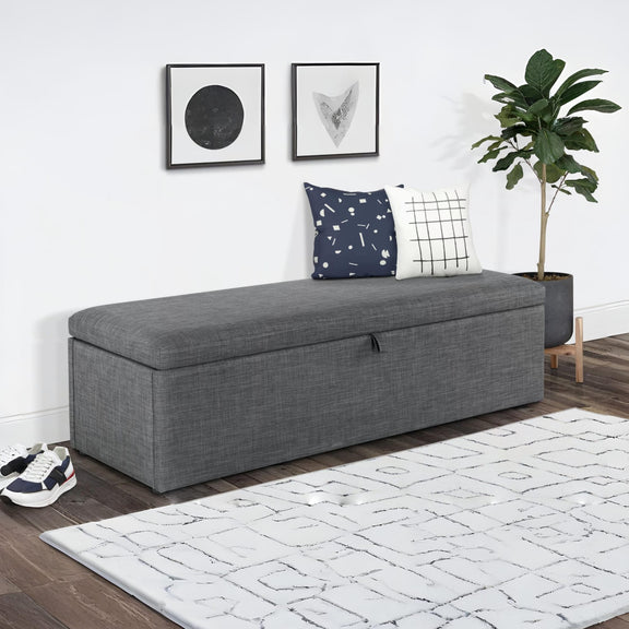 Gray upholstered bench with storage in a room with a rug, plant, and wall art.