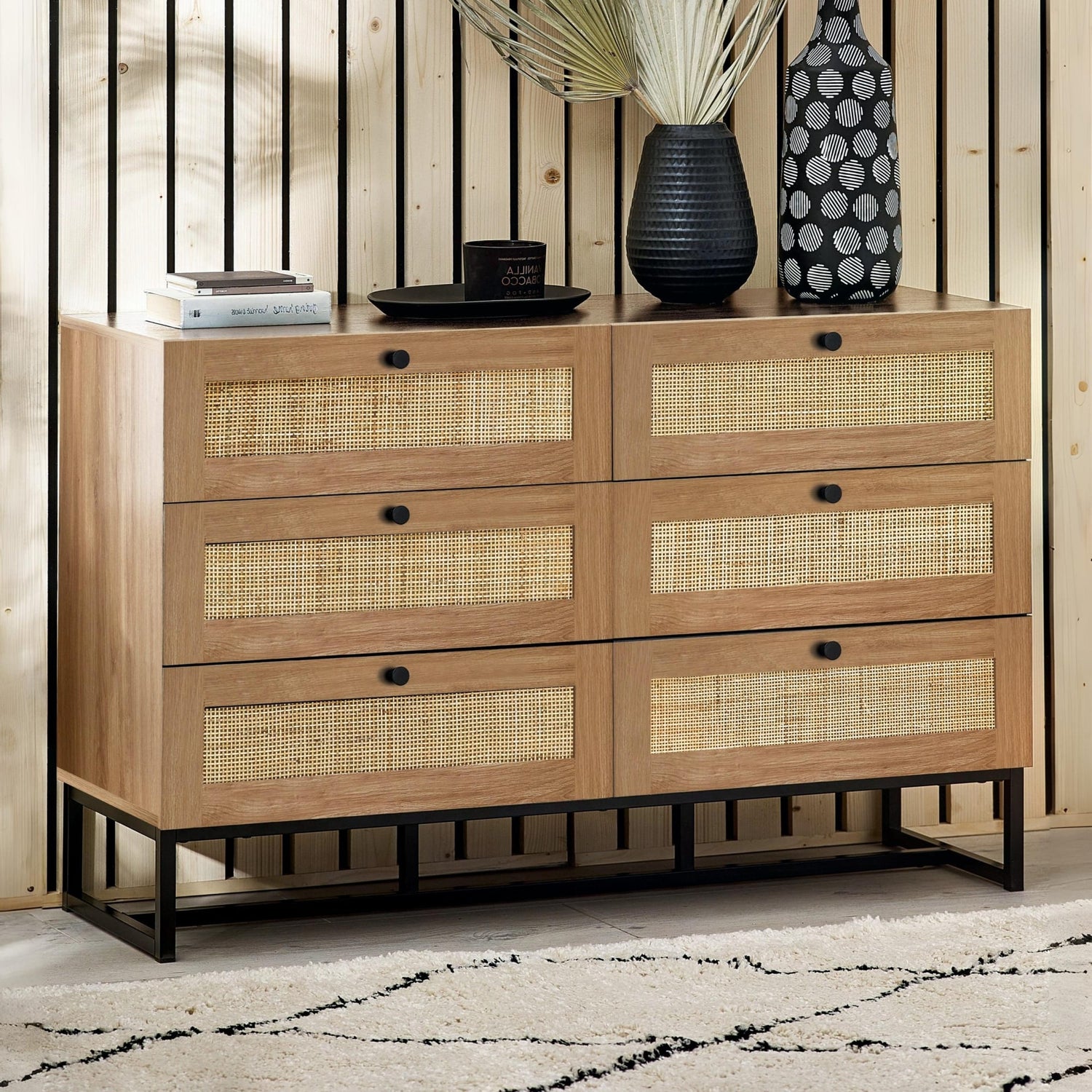 Wooden dresser with wicker drawers against a striped wall.