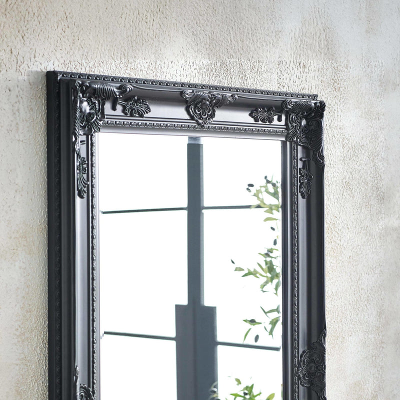 Decorative wall mirror with ornate black frame on a textured wall