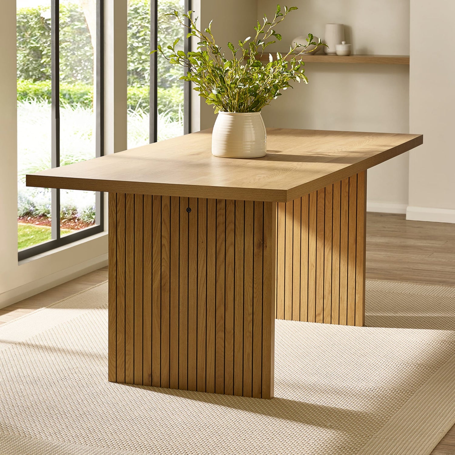 Wooden desk with a vase of greenery in a room with large windows.