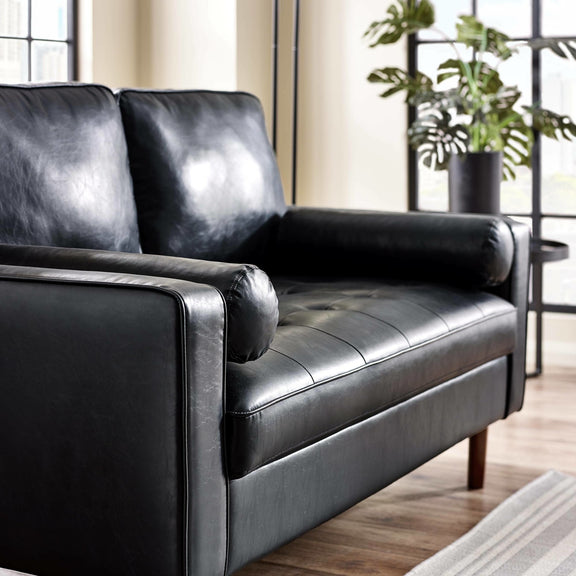 Black leather sofa in a living room setting with plants and a rug.