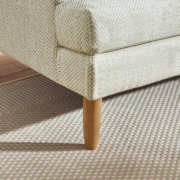 Close-up of a textured sofa corner with wooden leg on a patterned carpet