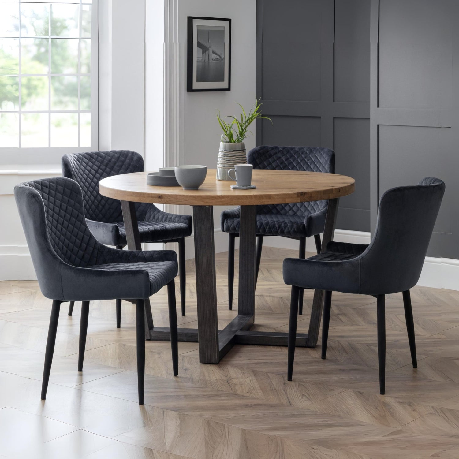 Dining room with a round wooden table and six dark chairs on a wooden floor.